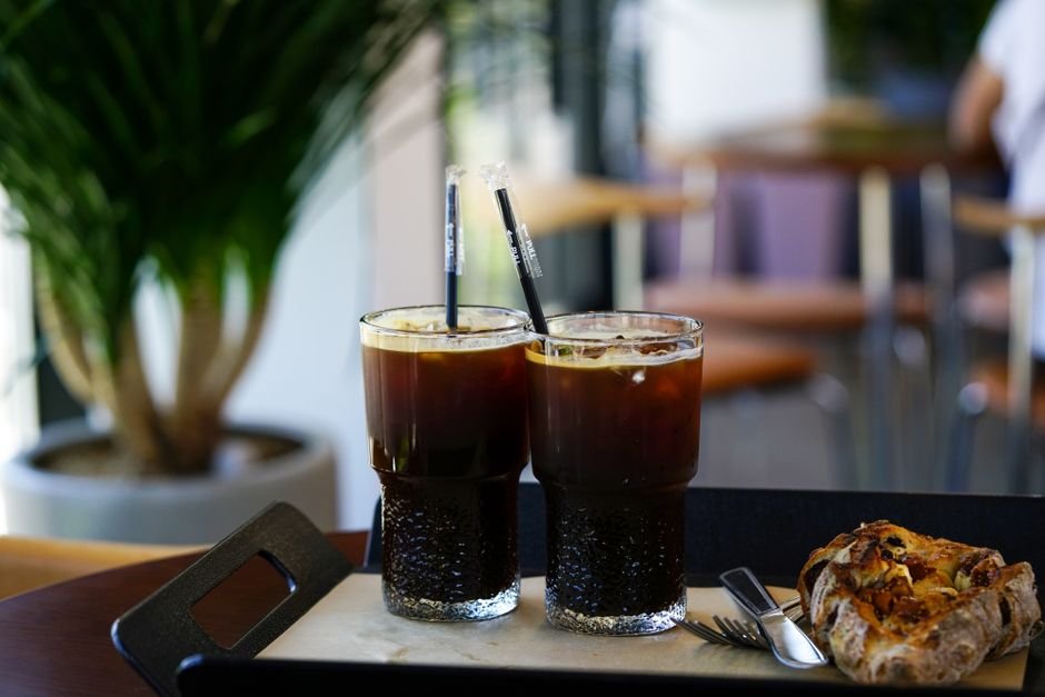 Two glasses of iced coffee with straws and pastry on a tray in a cozy cafe setting.