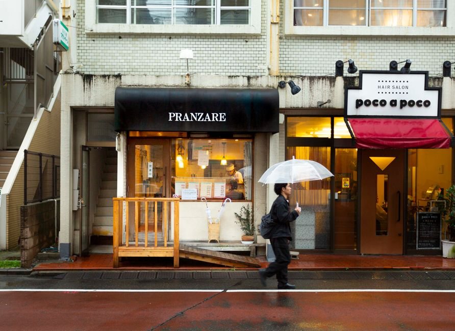 Pedestrian with umbrella passing by shops on a rainy day in Tokyo.